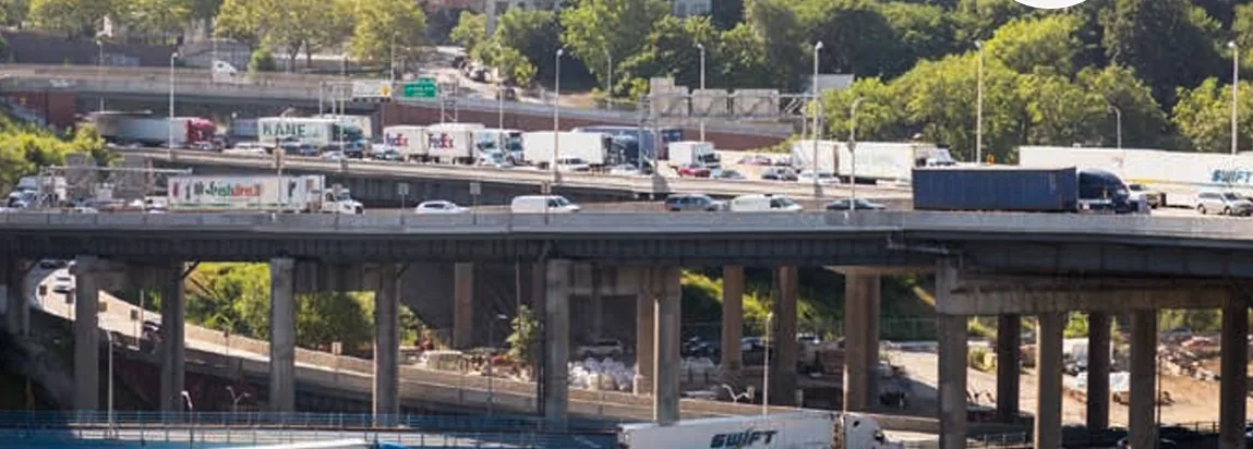 Tractor-trailers and cars fill the lanes of a multilevel urban highway.